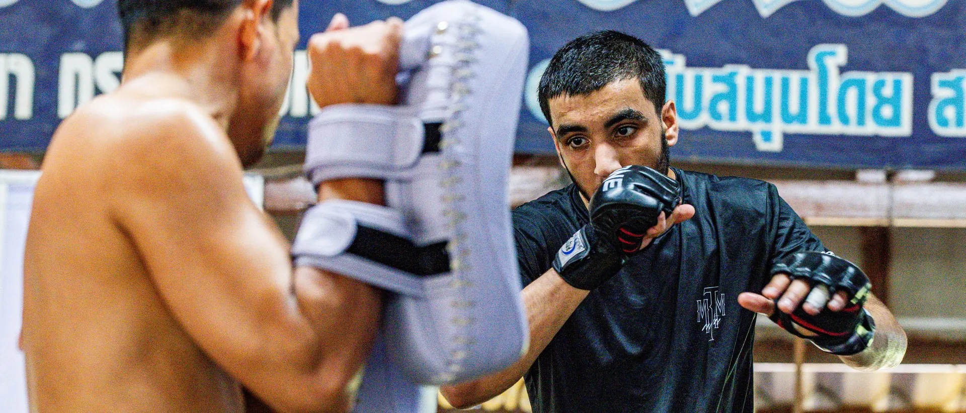 Student eyes-up over his gloves during a pad round at Kiatphontip Muay Thai camp, Bangkok