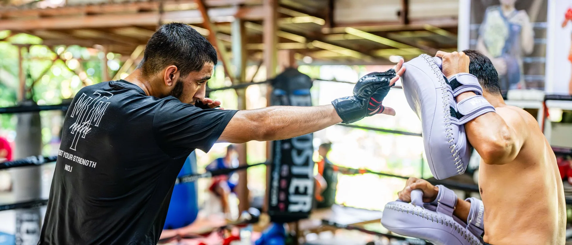 Student driving a punch into the pads during authentic Muay Thai training at Kiatphontip, Bangkok